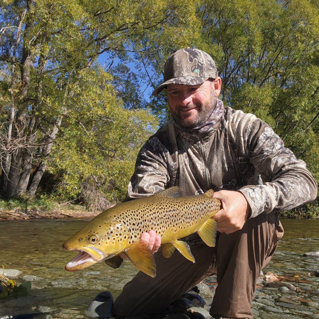 fisher holding a trout by the river